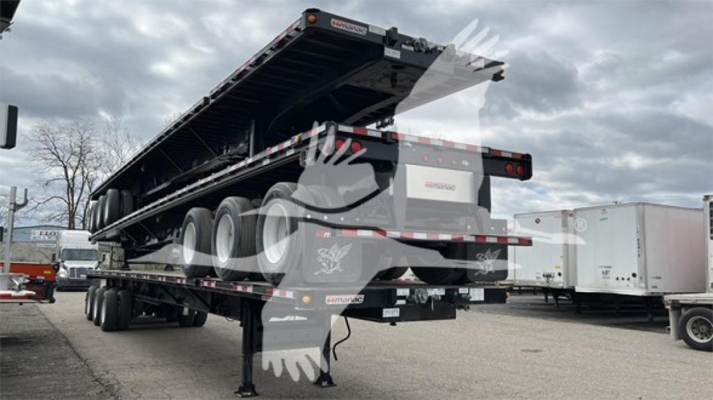 Manac extendable flatbed trailer viewed from rear-left, with multiple axles and a raised bed, loading ramps folded, warning labels and reflective tape visible.