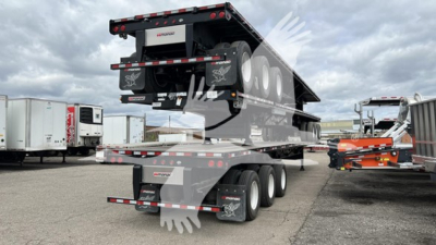 Manac extendable flatbed trailer in raised position with multiple axles and hydraulic extendable bed, visible tires and reflectors.