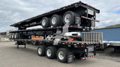 Manac extendable flatbed trailer showing multiple axles and a lowered center deck with reflectors and branding, side ramps, and rear extension components.