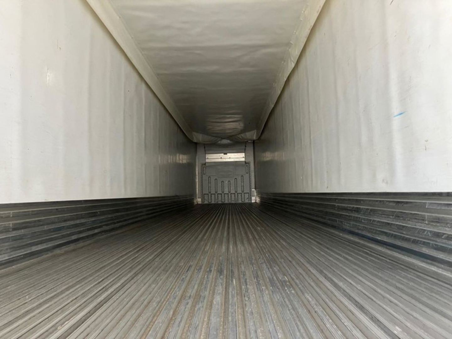 Trailer interior view of a refrigerated trailer with ribbed metal floor and white walls, looking toward the back doors.