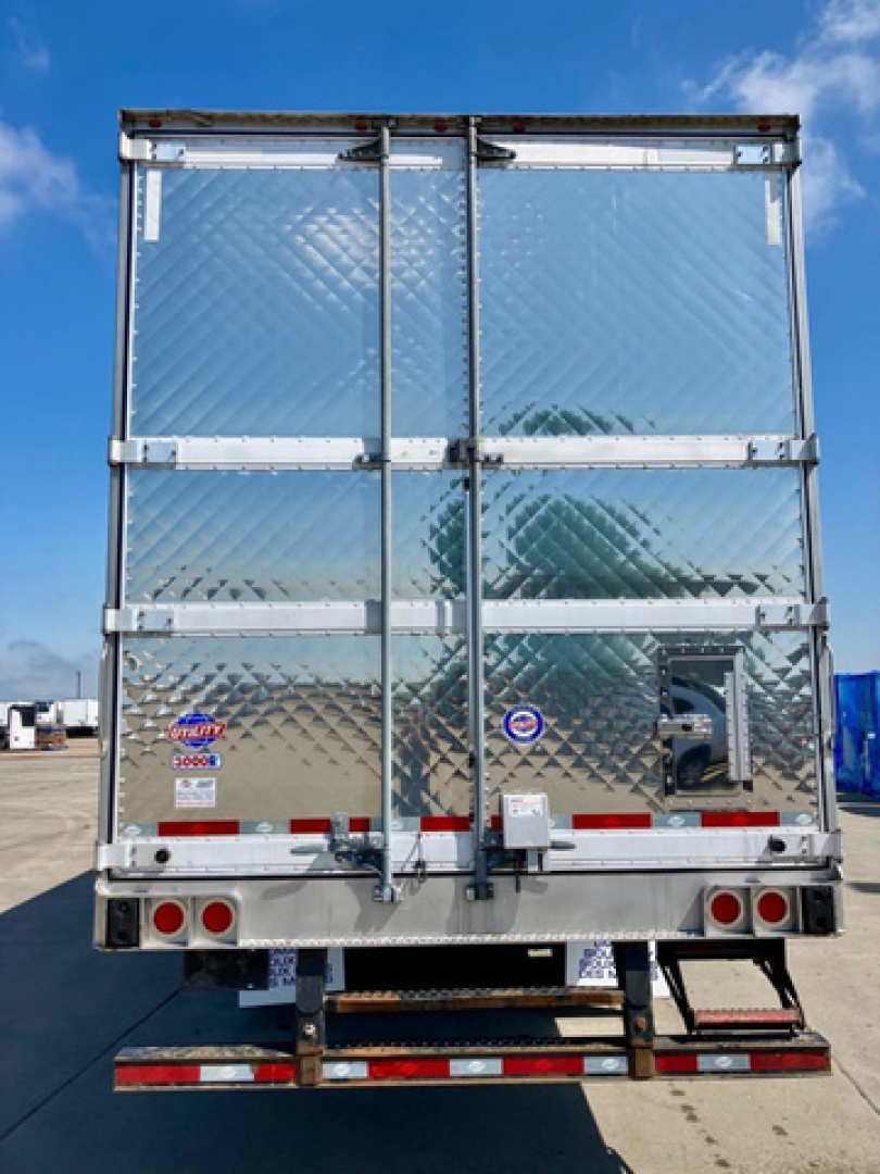 Rear view of a 2023 refrigerated trailer showing diamond plate doors and aluminum framing, with a metal bumper and red/white reflective markers.
