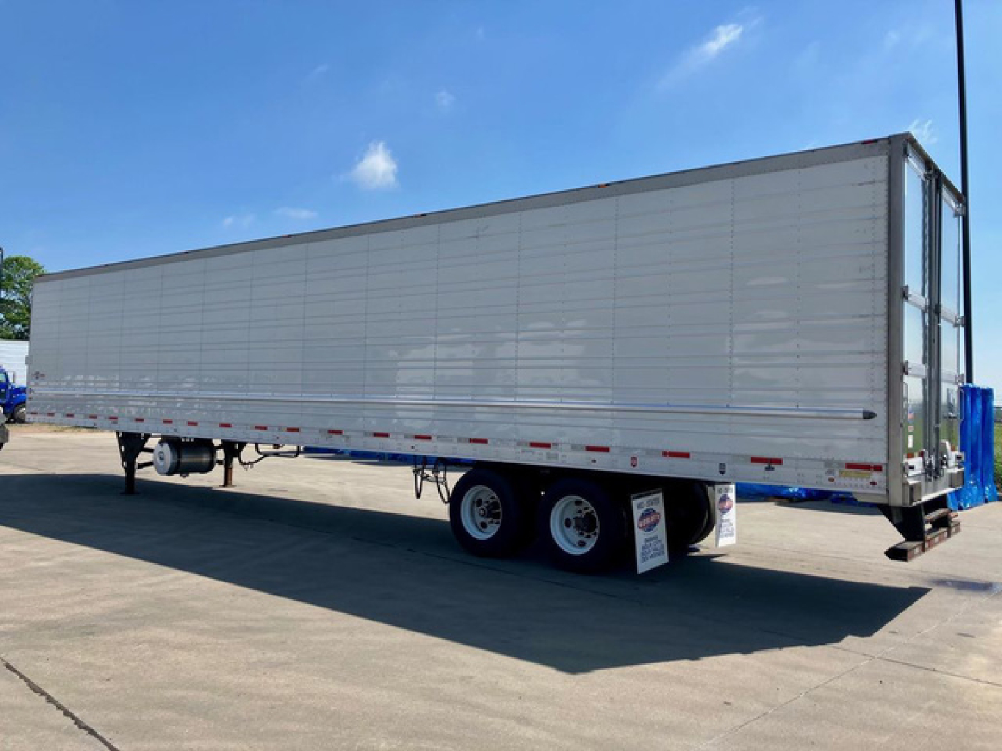 Trailer side view showing a 2023 Utility reefer trailer with long aluminum siding and dual rear axles under clear sky.