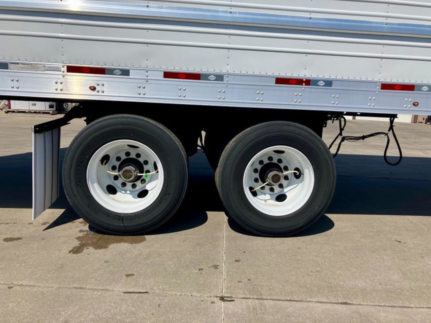Trailer wheels and tandem axles of a 2023 Utility Reefer trailer showing dual white rims and black tires, undercarriage with metal side rails.