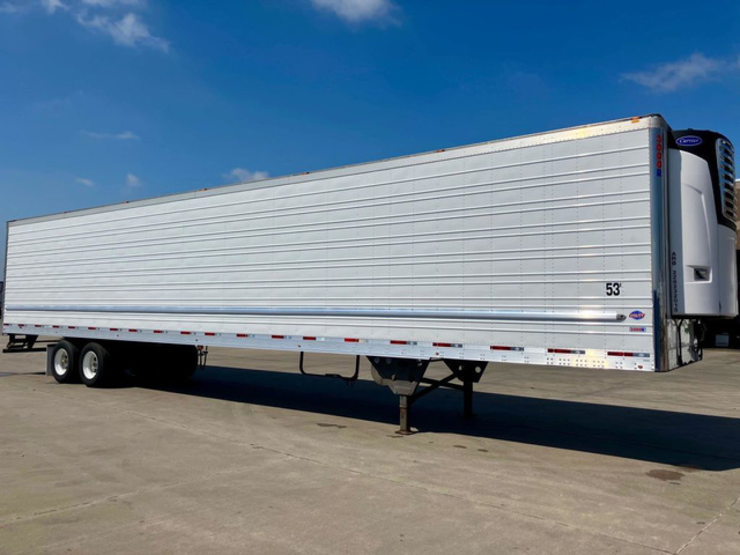Utility refrigerated trailer in side view with silver ribbed sides and a front refrigeration unit. Visible are tandem axles, landing gear, and reflective safety markings.