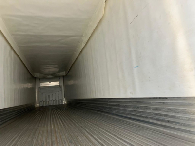 Interior of a refrigerated trailer showing corrugated metal floor and white walls, long narrow cargo hold with a rear door in the distance.