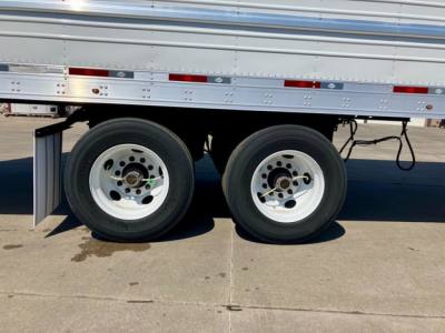 Trailer wheels and tandem axles of a 2023 Utility Reefer trailer showing dual white rims and black tires, undercarriage with metal side rails.
