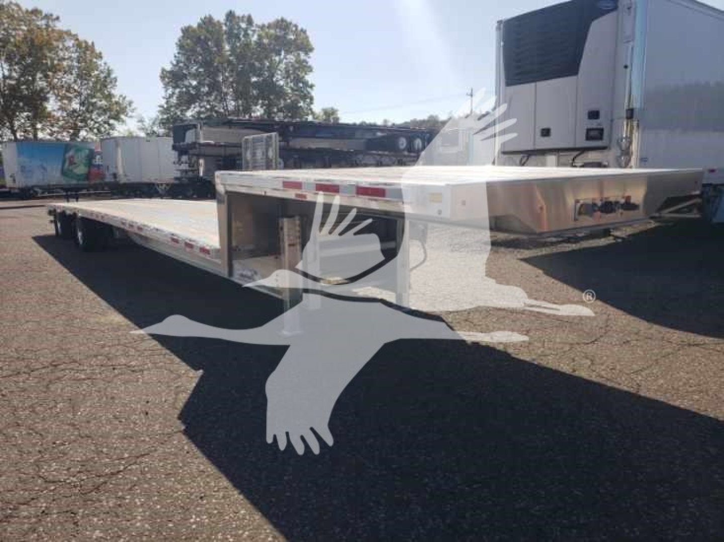Transcraft aluminum drop deck trailer viewed from front-left side showing long flatbed and shiny aluminum finish.