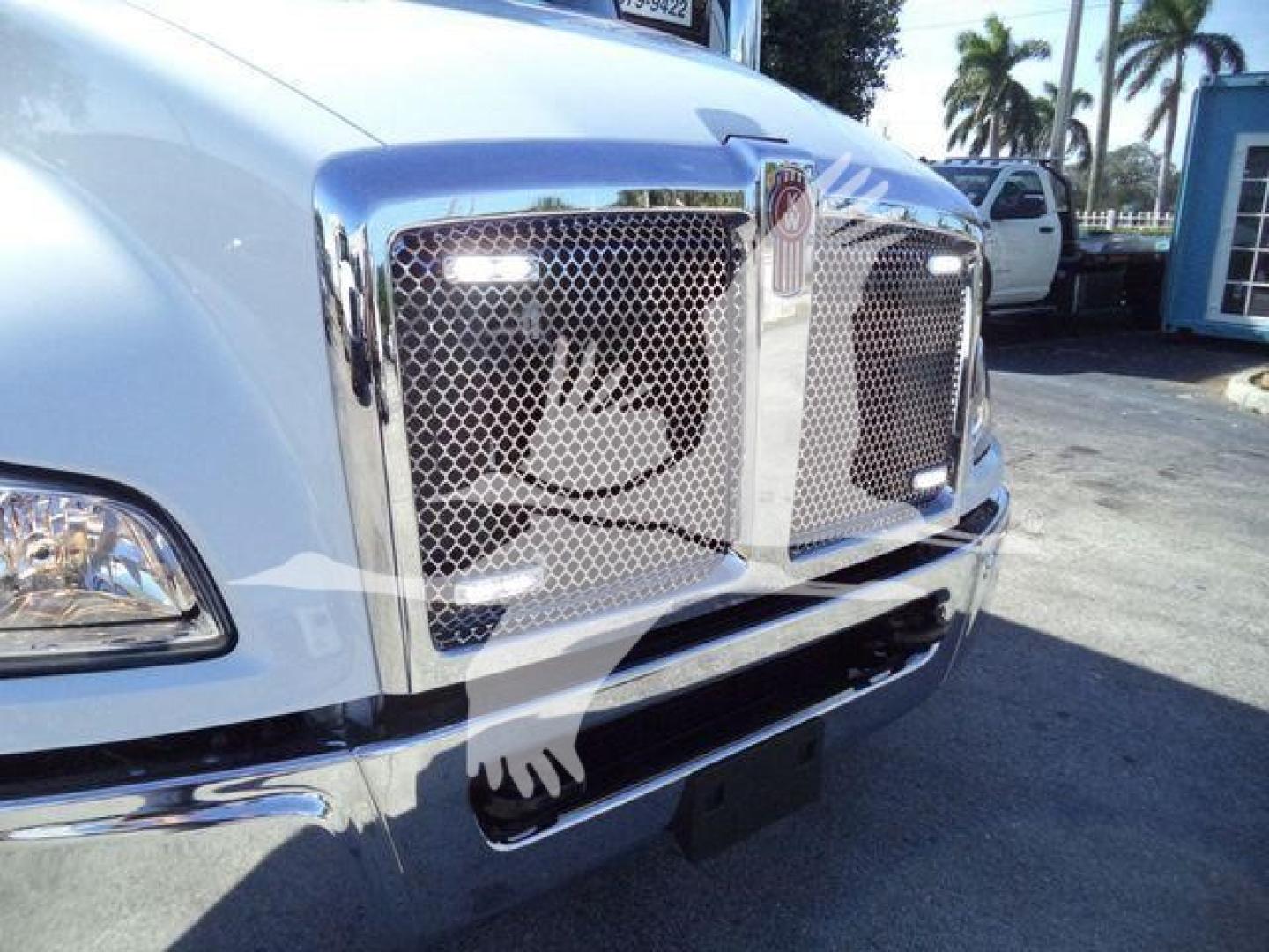 Front view of a white Kenworth truck with chrome grille and bumper, showing the front emblem and mesh grille.