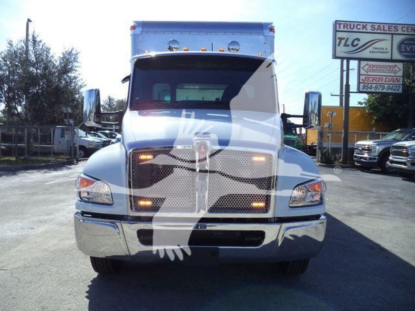 Front view of a white Kenworth T270/ T280 truck in a dealership lot showing headlights, grille, and hood. Visible text includes shop signs in background but focus on the truck front.