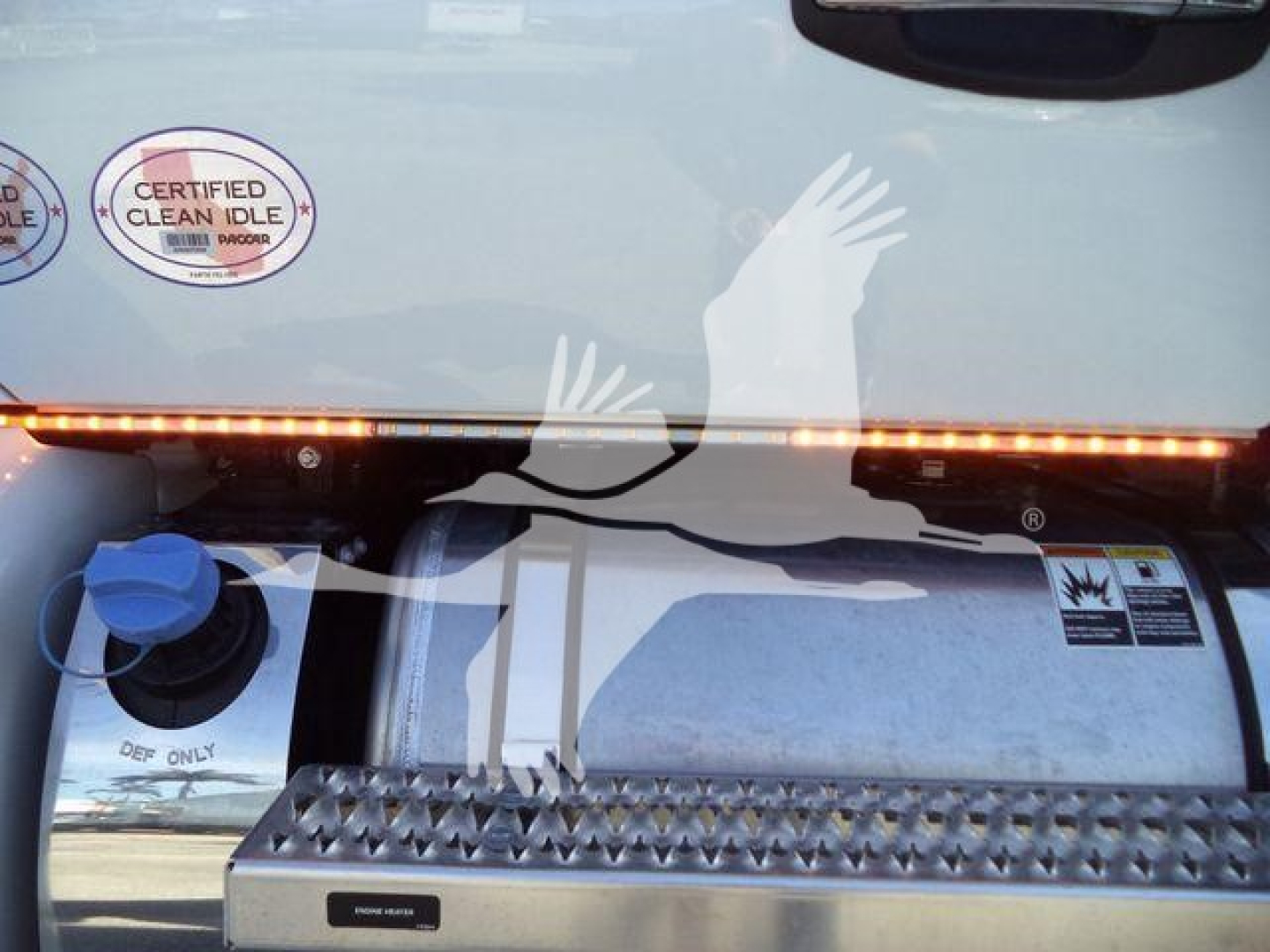 Truck fuel tank area with blue cap and metal diamond-plate step; Kenworth T280 in background with “Certified Clean Idle” sticker and safety decals visible.