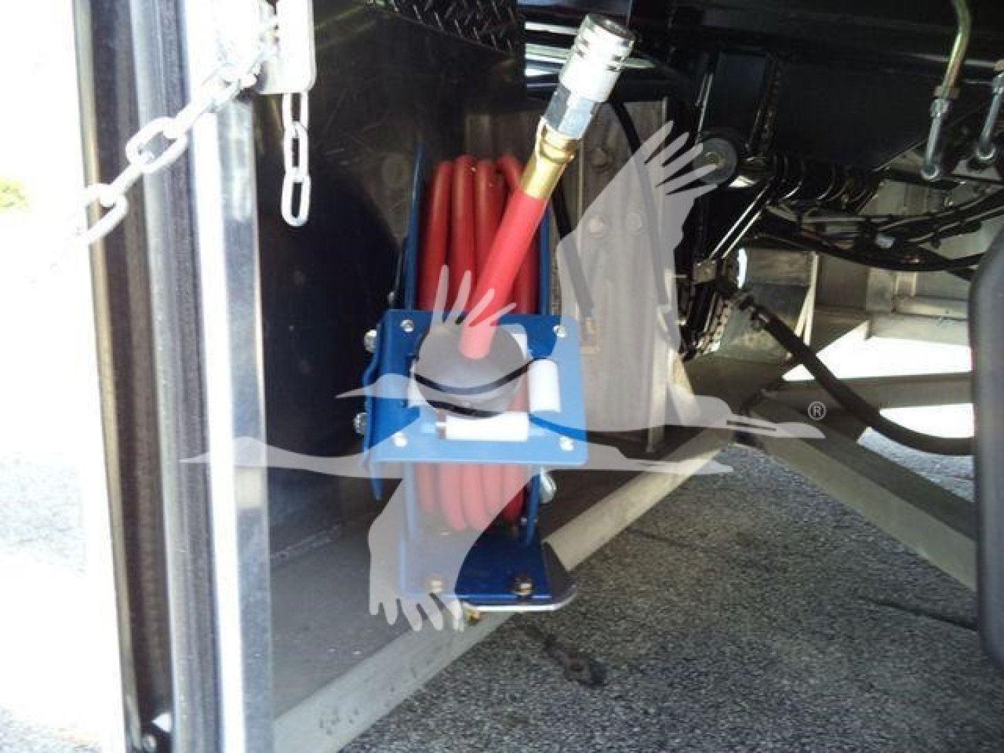 Kenworth equipment showing a coiled red hose with blue mounting bracket and hydraulic lines under a truck trailer; chain hangers visible.