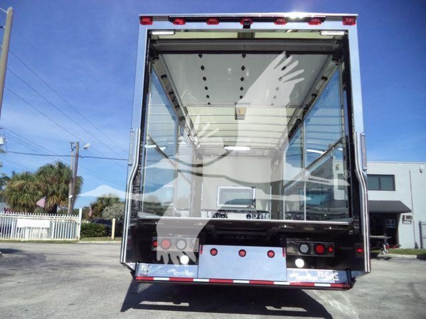 Rear view of a new Kenworth T280 rollback truck body with empty interior cargo space and open tailgate, reflective glass doors, and rear lights.