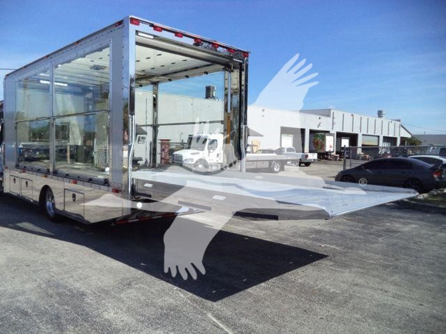 Kenworth T280 rollback truck with a large front-loading ramp and glass sides, showroom in background.