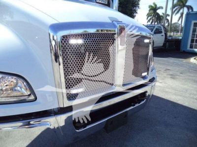 Front view of a white Kenworth truck with chrome grille and bumper, showing the front emblem and mesh grille.