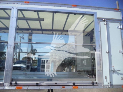 Kenworth T280 rollback truck cab rear window with metal frame and glass panels, reflection of surroundings visible.