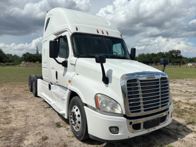 Semi truck cab in white with large chrome grille from a Freightliner Cascadia Evolution, front-right view, daytime outdoor setting
