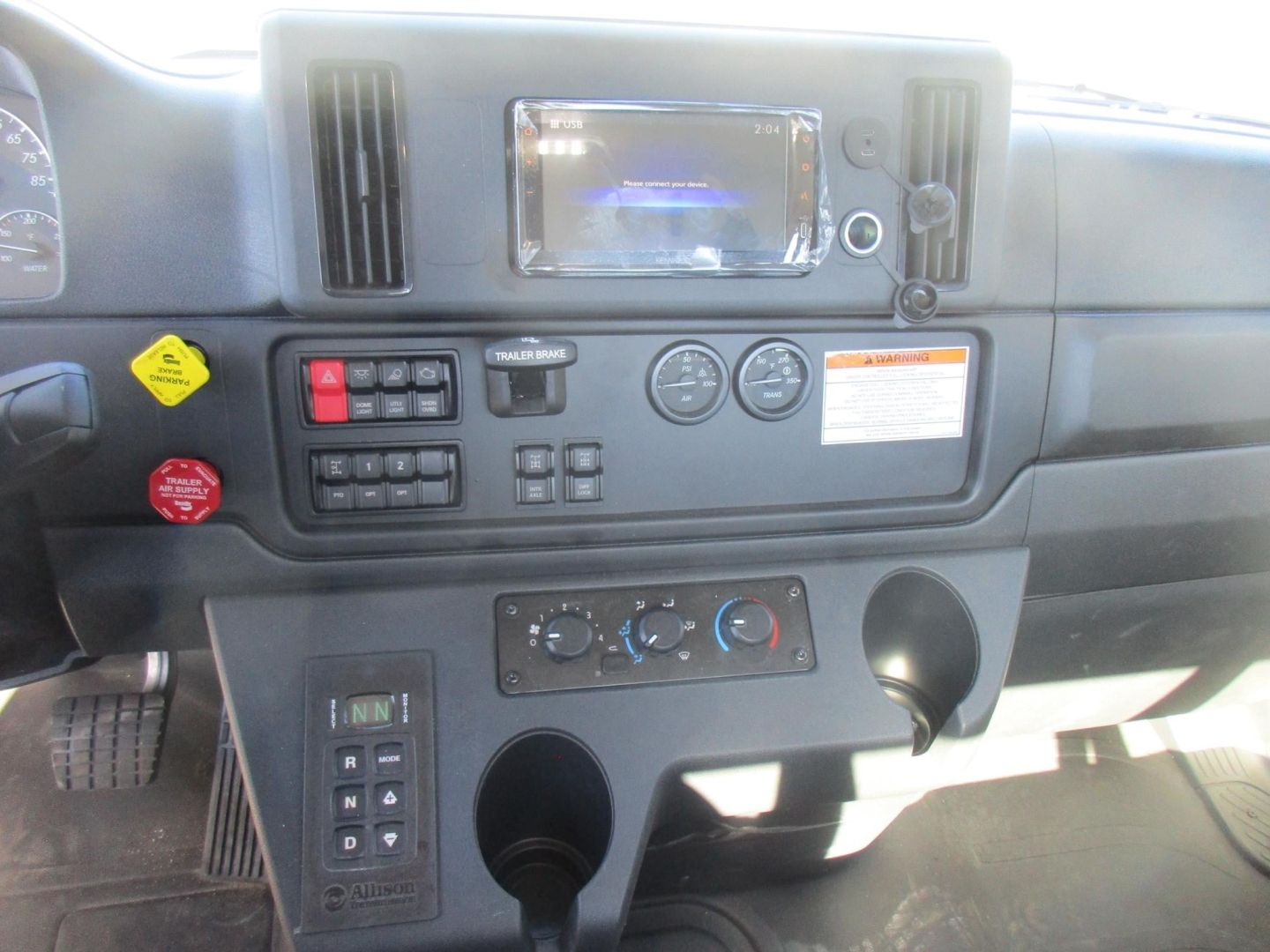 Dashboard view of a Freightliner M2 106 Plus cab and chassis showing center touchscreen display, climate controls, switches, and gauges.