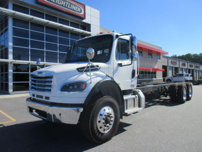 Freightliner M2 106 Plus cab and chassis truck in front of dealership, silver/white with chrome bumper and dual rear axles, VIN 3ALHCYFE2VDXG0103.