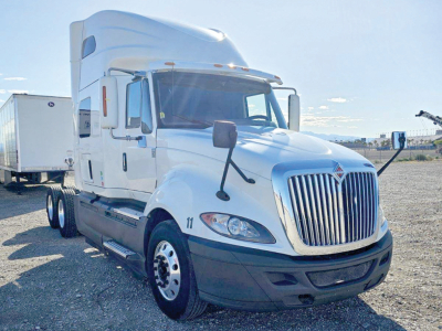 Truck cab with attached sleeper, International LT625 model, white with chrome grille and dual rear axles visible, side mirror views, dealership lot.