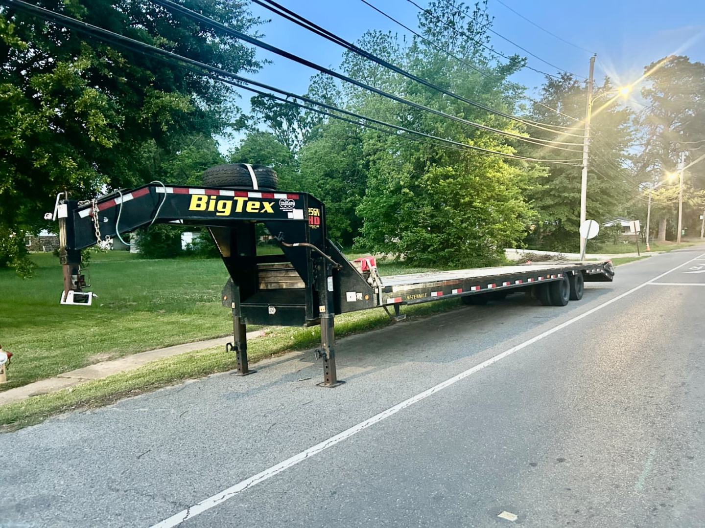 Big Tex flatbed trailer with gooseneck neck, black frame, yellow BigTex logo, long dual-axle deck, parked on street.