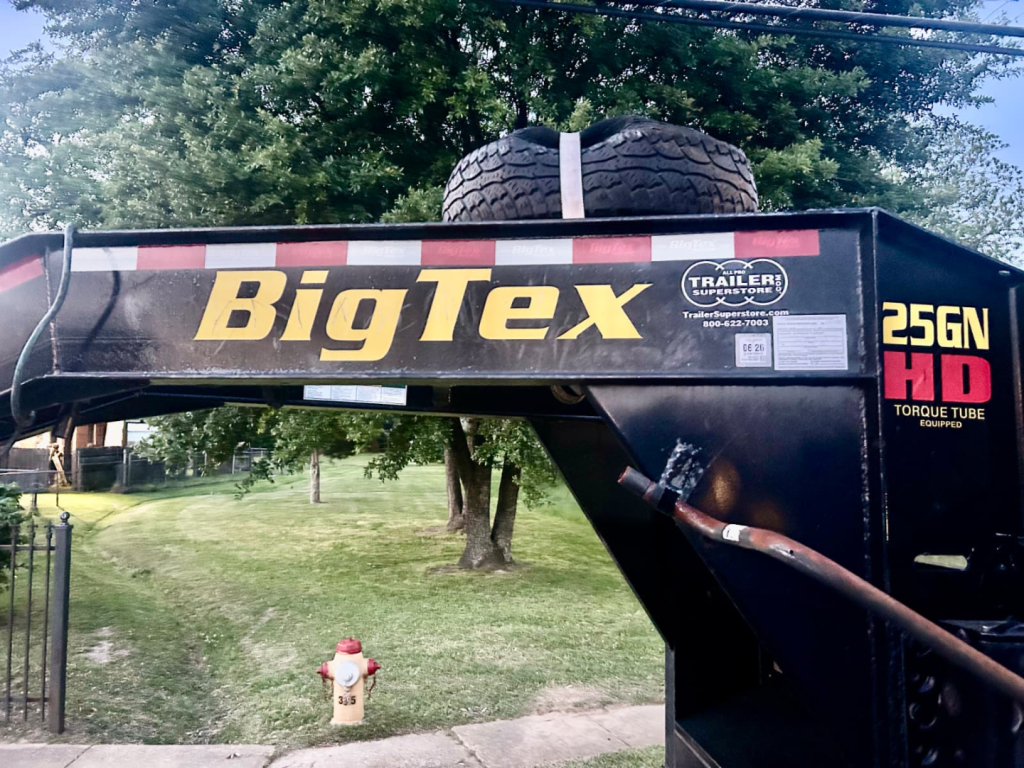 BigTex 25GN-40D5A-MRBK trailer with large BigTex logo, flatbed gooseneck, and spare tire mounted on top, side shows 25GN 40D5A model label.