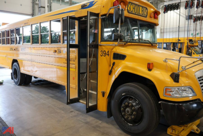 Yellow 2018 Blue Bird Vision school bus inside a shop showing open door, front wheels, and 'SCHOOL BUS' sign on hood.