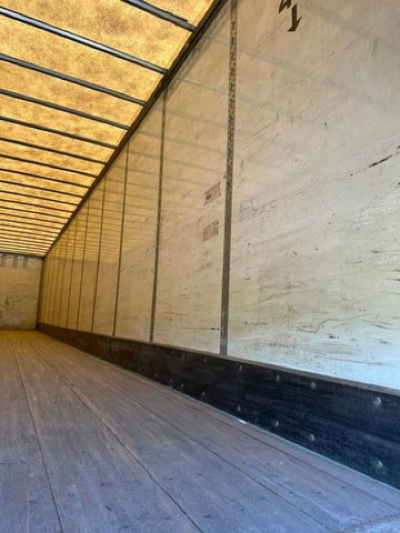 Trailer interior: wooden floor and white side walls, cargo trailer with ribbed ceiling beams seen along length.