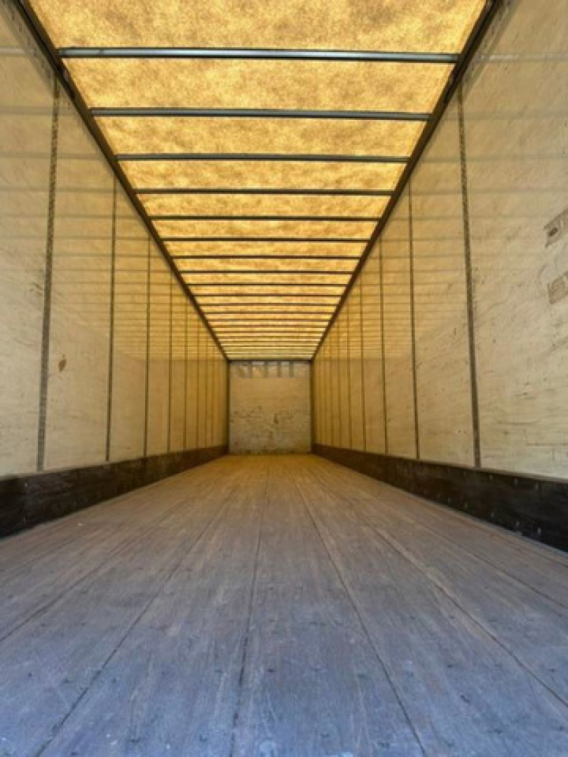 Truck trailer interior showing long empty cargo area with wooden floor, side walls, and exposed ceiling framing.