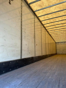 Trailer interior showing empty cargo space with wooden floor, side walls, and ribbed ceiling.