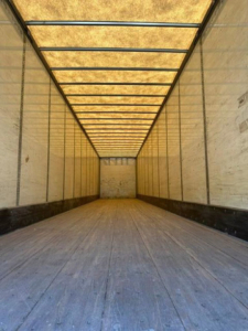 Truck trailer interior showing long empty cargo area with wooden floor, side walls, and exposed ceiling framing.