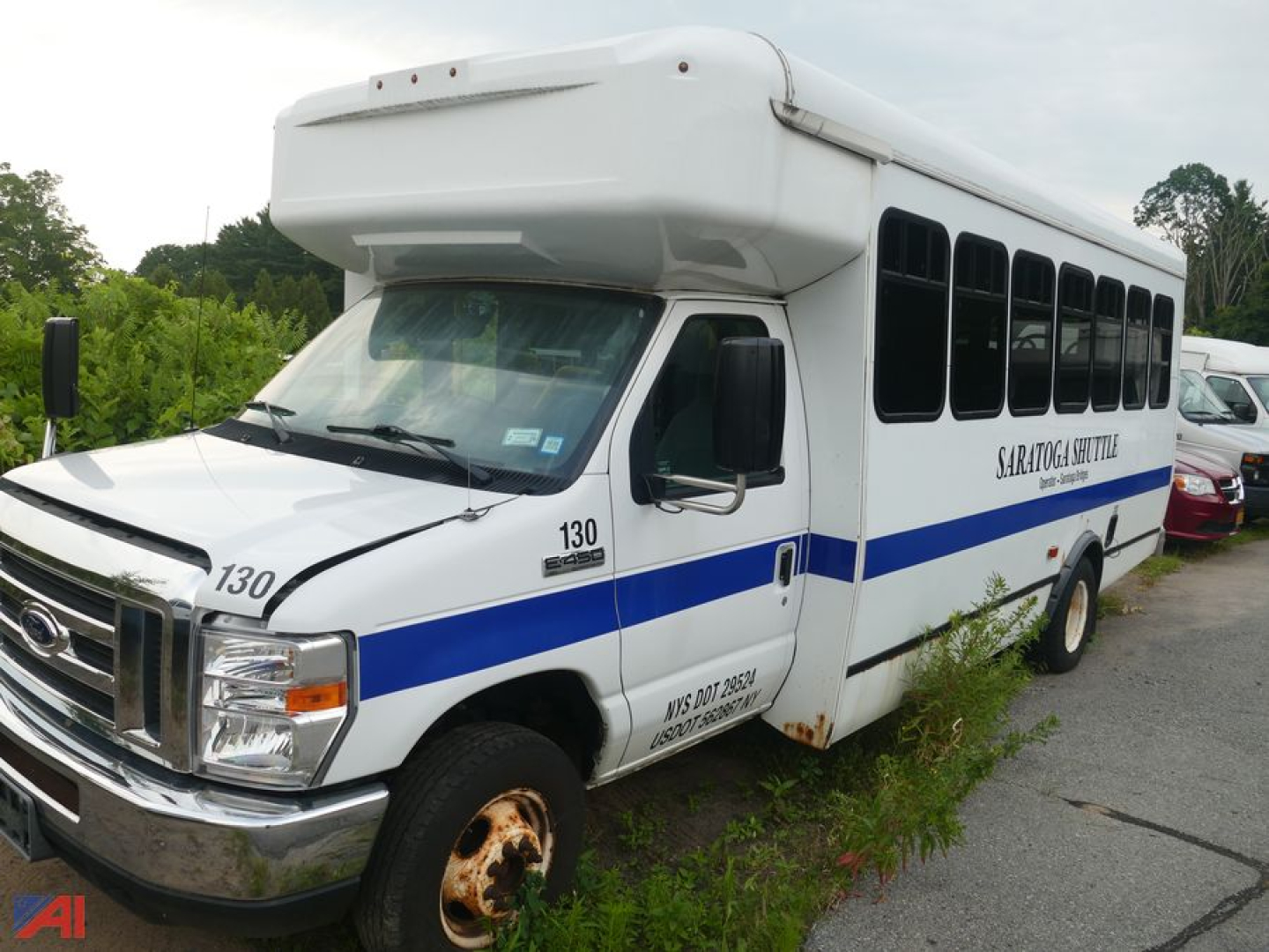 Ford Econoline E-450 shuttle bus with wheelchair lift, white with blue color stripe, sliding side windows, front chrome bumper, bus number 130, visible rust on front wheel area.