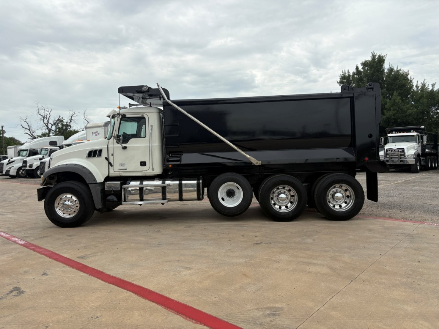 Dump truck side view showing 2021 Mack GR64F with black dump bed and white cab.
