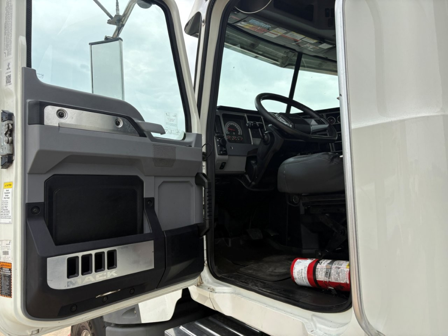 Truck cab interior visible through open door of 2021 Mack GR64F dump truck showing steering wheel dashboard and door panel with black and silver accents.
