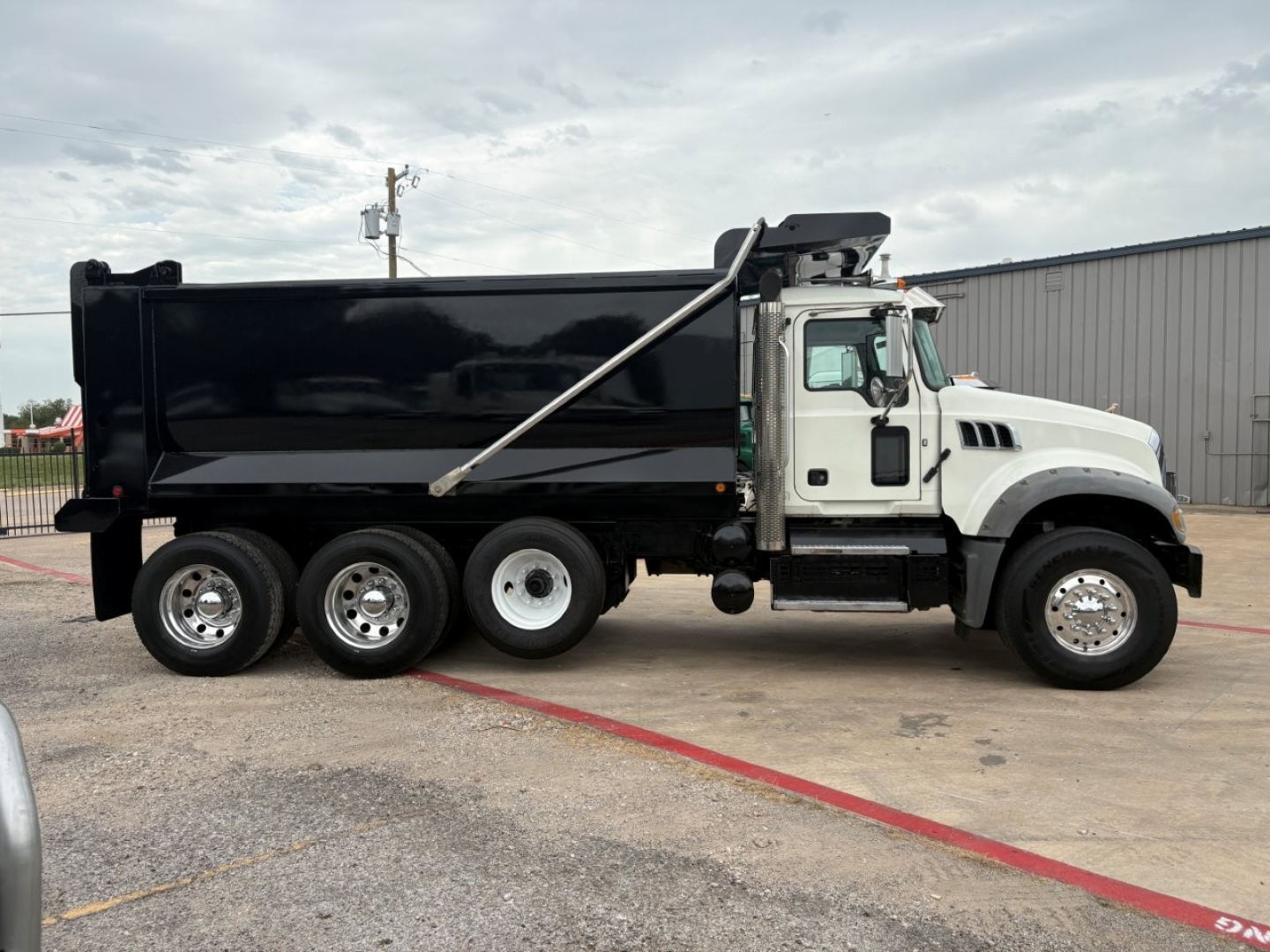 Dump truck side view showing a white cab with black dumping bed and multiple rear axles.