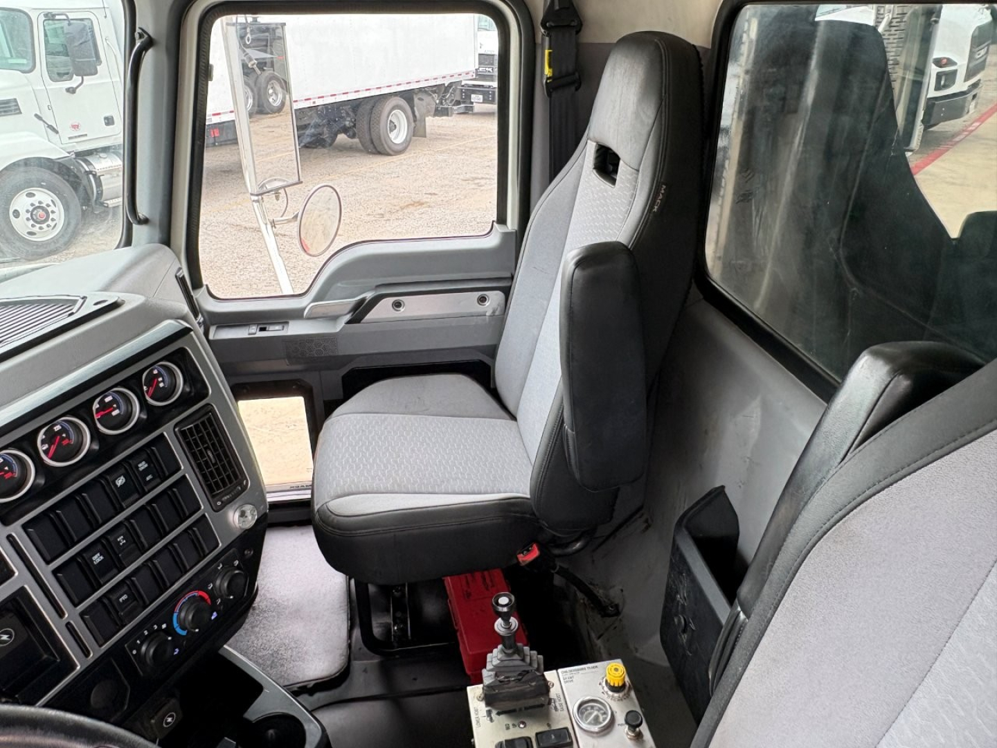 Truck cab interior of a 2021 Mack GR64F showing driver's seat, dashboard with gauges, and passenger seat. Visible gear selector and control panels.