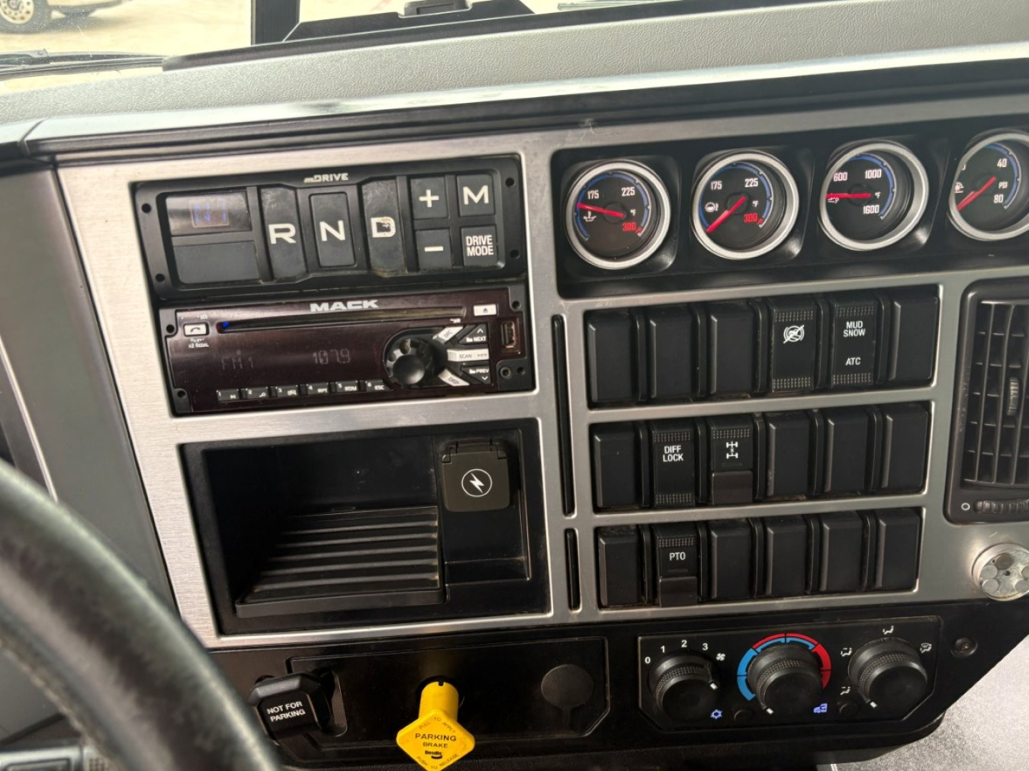 Dashboard of a 2021 Mack GR64F showing gear selector (R N D M), multiple gauges, radio, and climate controls.