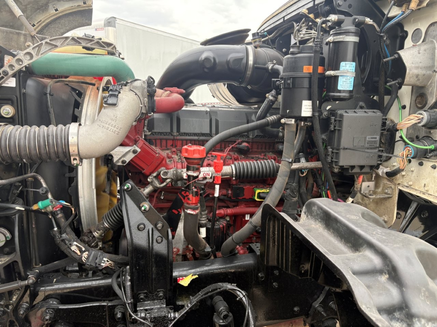 Truck engine bay showing Mack GR64F diesel engine with red engine block, hoses, and various components including coolant hoses and air intake.