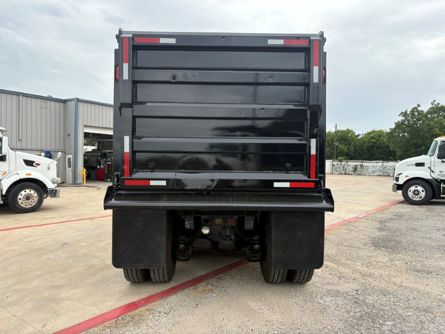 Dump truck bed rear view showing Mack GR64F with black dump bed, taillights, and rear wheels visible.