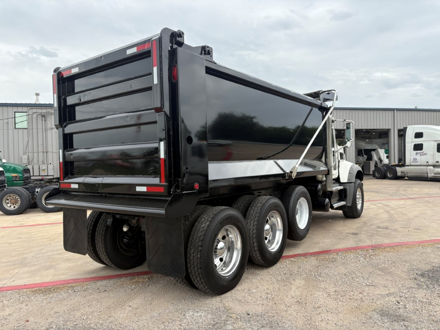 Dump truck with 3-axle rear, black dump body, white cab, side view showing rear wheels and hydraulic mechanism.