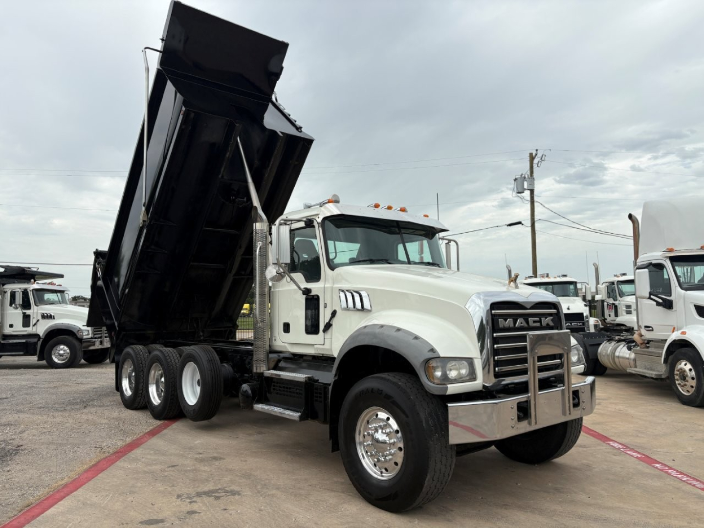 Mack GR64F dump truck with raised dump bed, front grille showing Mack emblem, white cab, dual rear axles, chrome bumper, Load-rated tires.