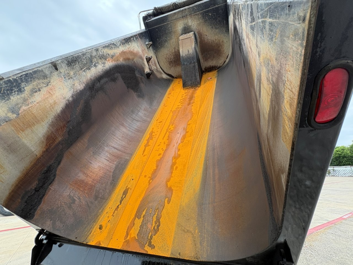 Dump truck bed side with orange painted stripe and metal wear inside; Mack GR64F chassis area visible.
