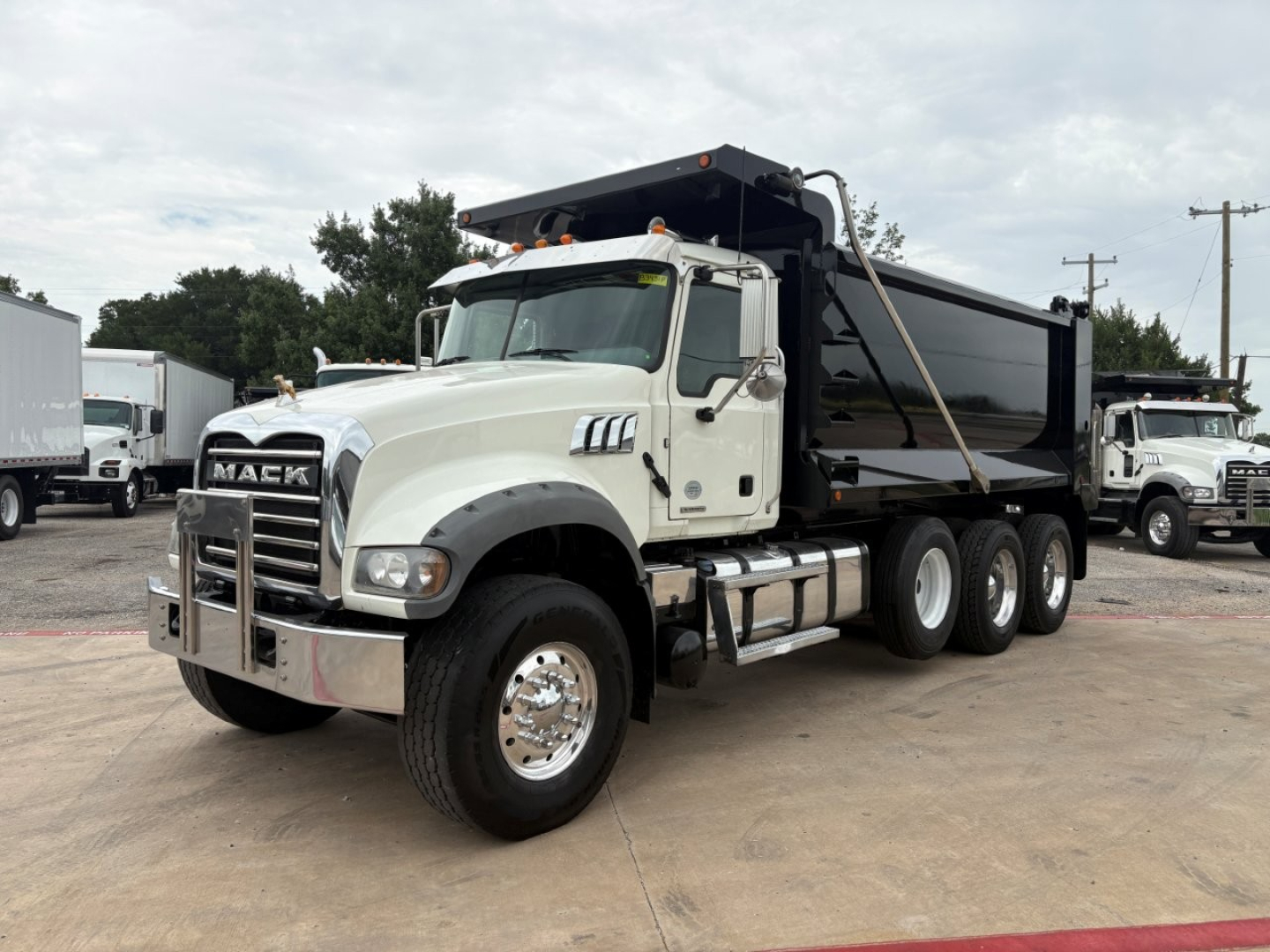 Mack GR64F dump truck in side view showing white cab and black dump body with tandem rear axles.