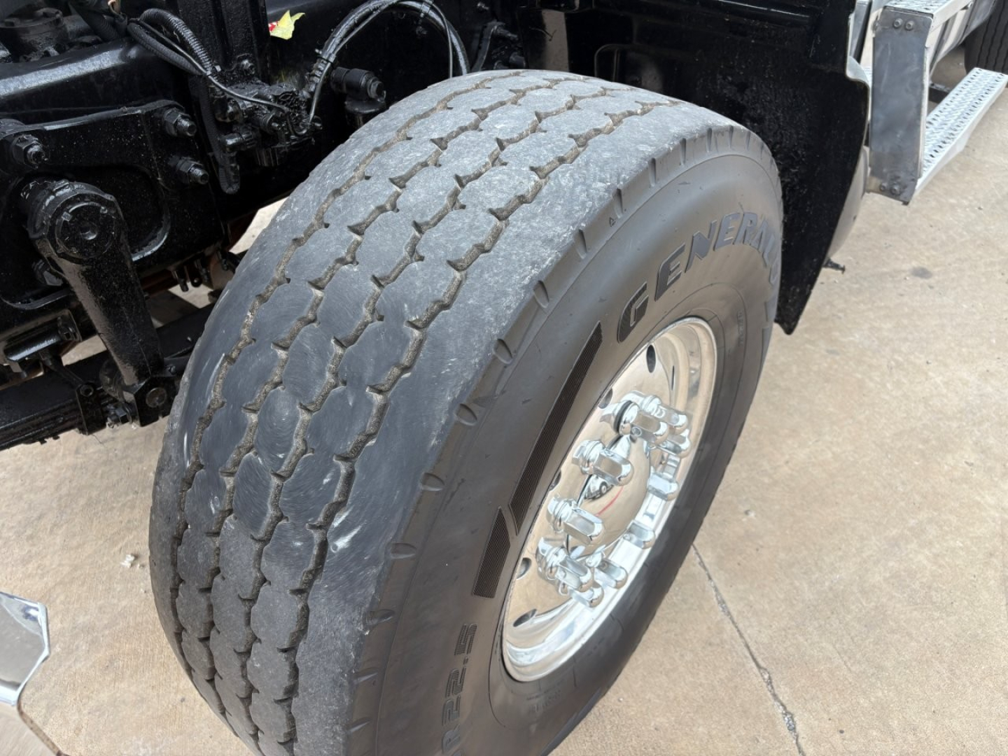 Front wheel and tire of 2021 Mack GR64F dump truck showing Goodyear or generic tire with chrome rim and suspension components visible.