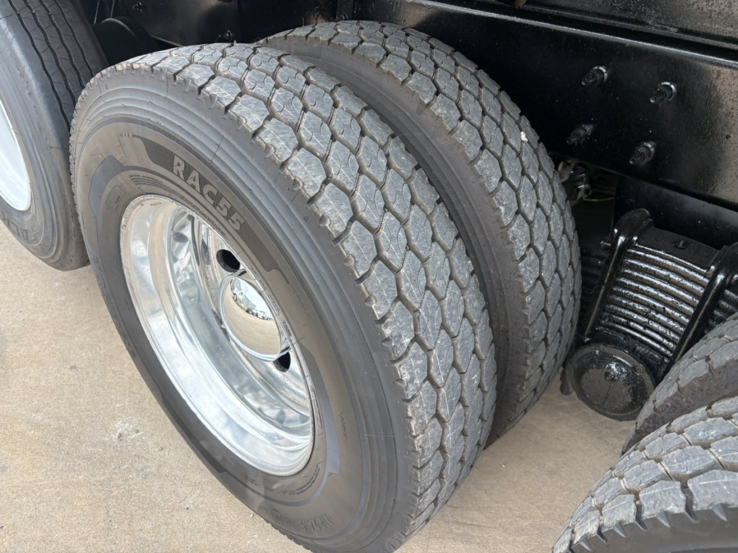 Dual rear wheels on a Mack GR64F dump truck showing tire tread and chrome rims with suspension components nearby.