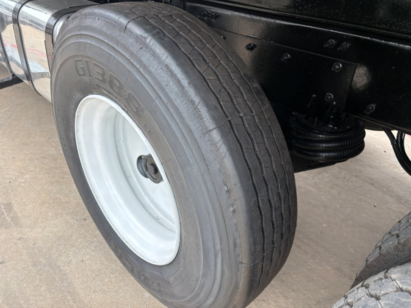 Mack GR64F dump truck rear wheel showing tire and white wheel rim with suspension components visible.