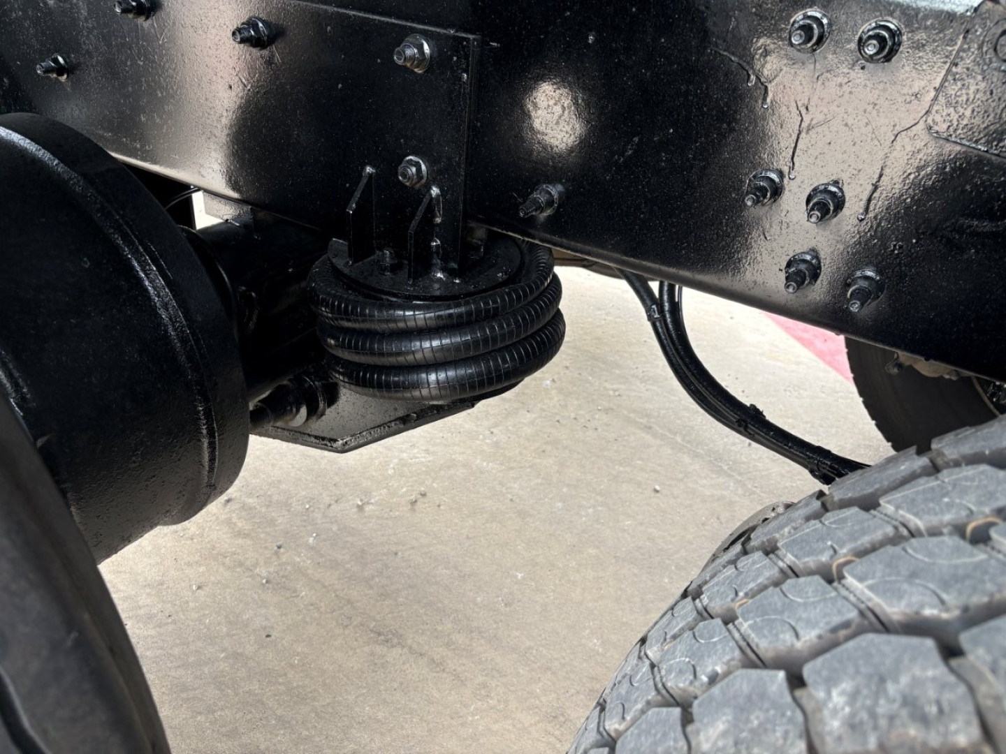 truck frame and suspension near a rear wheel showing leaf spring stack and axle housing with black painted metal components.