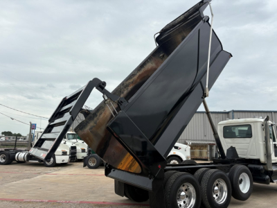 Truck dump bed raised on a Mack GR64F chassis with dual rear axles and black dump bed, side view showing metal framework and hydraulic components.