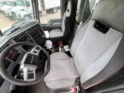 Truck cab interior of a 2021 Mack GR64F showing steering wheel, dashboard with gauges, and driver seat with light gray fabric. Visible control panel and center console.