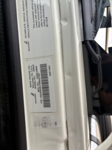 Label stickers on door jamb of a 2021 Mack GR64F dump truck showing VIN and serial/barcode text.
