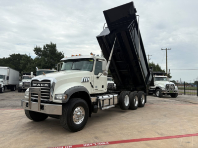 Mack dump truck with a raised black dump bed, white cab, chrome bumper and grille. Visible on the truck: Mack emblem on the grille; side mirrors; dual rear axles with heavy-duty tires. No legible serials or additional text visible.